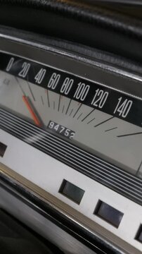 A detailed close-up of a vintage analog car speedometer featuring a bright orange needle. The classic vehicle dashboard includes a mechanical odometer and textured black trim.