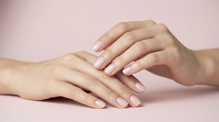 Fototapeta premium Gentle touch of two feminine hands with natural unpolished nails on a soft pink background.