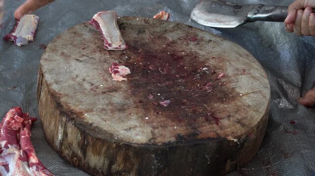 A butcher chopping raw meat on a large wooden cutting board