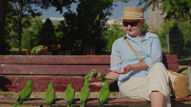 Woman feeding monk parakeets while sitting on bench in Ciutadella Park near Arc de Triomf in Barcelona