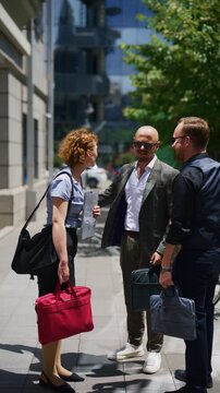 Three business professionals engage in a lively outdoor discussion, reviewing documents together. Colleagues hold an impromptu meeting outside, collaborating in a modern urban environment.