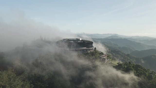 Aerial view of a modern circular building on a lush mountain peak shrouded in thick white fog and clouds Cebu City, Central Visayas, Philippines.