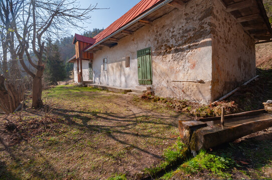 View of the historic Prasnica old charcoal burners' settlement with a traditional white stone house and wooden water trough Stare Hory, Banskobystricky kraj, Slovakia.