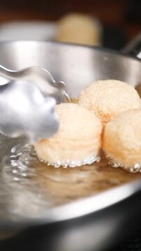 Chef friendo pani puri en sart&eacute;n de acero inoxidable (primer plano). Un chef profesional fr&iacute;e pani puri crujiente en una sart&eacute;n de acero. Comida callejera india, receta tradicional.