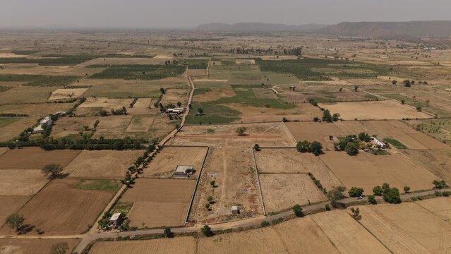 View of the Naugaon rural landscape with agricultural fields, scattered buildings and distant hills under a hazy sky in Naugaon, Rajasthan, India.
