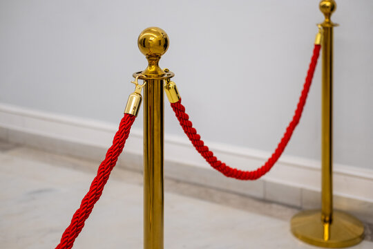 Gold stanchion post with a twisted red velvet rope barrier on a light marble floor, indicating VIP access or a restricted queue.