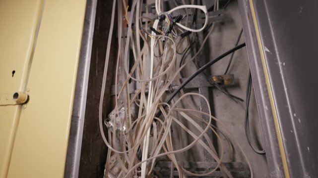 Tangled cluster of white telecommunication wires fills an open dusty utility cabinet. Vertical camera tilt reveals chaotic cable management and debris inside the yellow metal enclosure.