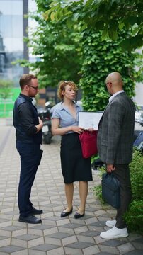 Three diverse business colleagues hold a professional outdoor discussion, reviewing documents. They collaborate and communicate effectively during this impromptu urban meeting.