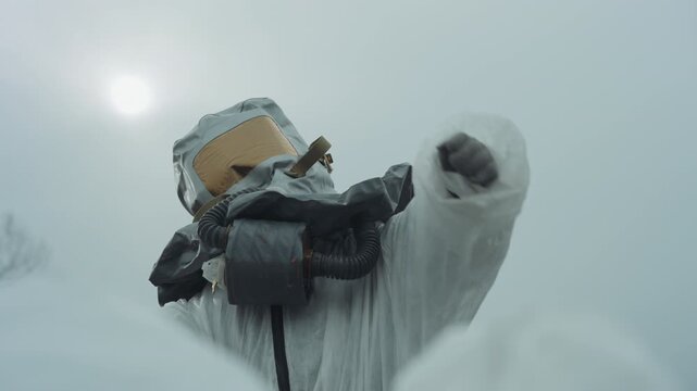 Scientist in hazmat suit kneeling over snow, examining ground for contamination, adjusting respirator, scanning sample with gloved hands, visor reflecting pale winter sun, abandoned industrial