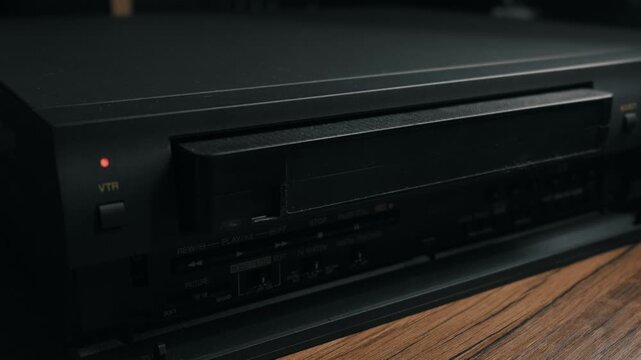 A hand presses the eject button on a retro video cassette recorder and pulls out a black VHS tape. Concept of vintage technology, nostalgia for the 90s, and watching old home movies.