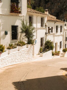 View of traditional white-washed houses with flower pots and black iron grates along a narrow sunlit street Zuheros, Andalusia, Spain.