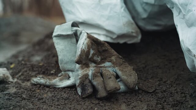 Dirty glove lying on muddy ground, cuff of white protective suit visible, soilcovered textile detail, silent evacuation aftermath, investigative tension and weathered abandonment