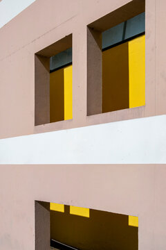Pink facade turns yellow windows into minimal geometry, where shadow cuts across the building wall and architecture reads as bold color blocks