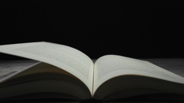 An open book displays pages turning and flipping in mesmerizing slow motion against a deep black background. This visual concept embodies knowledge, education, learning, and the art of