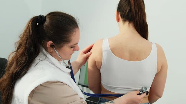 Family doctor uses stethoscope to checks woman lungs at clinic appointment slow motion. Female physician listens to patient breathing in hospital