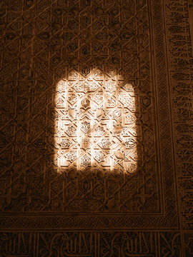 View of intricate Islamic geometric carvings and Arabic calligraphy on a wall with a patch of sunlight in the Alhambra Granada, Andalusia, Spain.