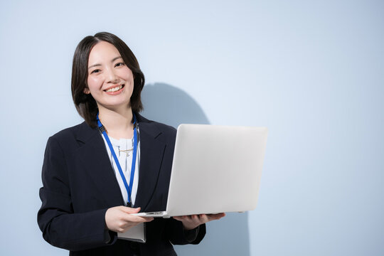 水色背景で名札をつけたノートパソコンを持つ働くかわいい女性社員のビジネスとITなどのイメージ　カメラ目線の笑顔 右にコピースペース