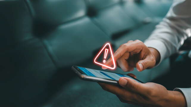 Hand holding smartphone with glowing red warning triangle icon overlay signifying danger or alert on screen.