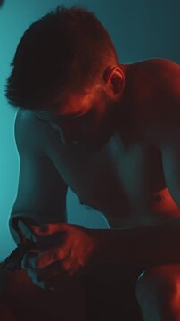 Focused male athlete resting and preparing between intense functional training exercises in a low-lit gym environment, highlighting dedication, strength, and concentration