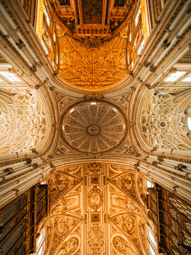 View of the ornate golden vaulted ceiling and central dome of the Mosque-Cathedral with intricate carvings and Renaissance architecture in Cordoba, Andalusia, Spain.