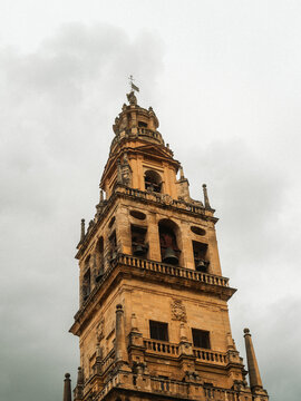 View of the ornate bell tower of the Mosque-Cathedral of Cordoba with its intricate stone carvings and bells against a cloudy sky Cordoba, Andalusia, Spain.