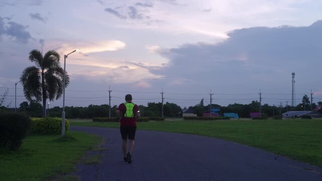 Middle-aged Asian man jogging safely at twilight with reflective gear and LED arm light