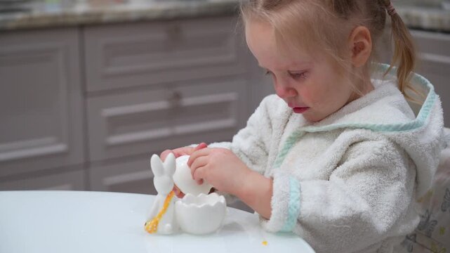 Upset toddler crying while peeling boiled egg in kitchen setting during holiday morning activity