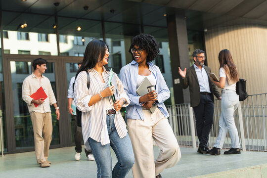 Two happy Asian African American students girls walking and talking in University campus after classes, going out of college
