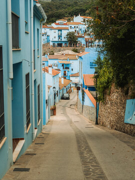 View of a narrow street lined with blue-painted houses and terracotta roofs in the village of Juzcar, Andalusia, Spain.