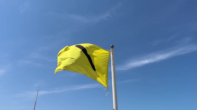 Yellow beach warning flag with black symbol waving in the wind against a clear blue sky indicating medium hazard for swimmers