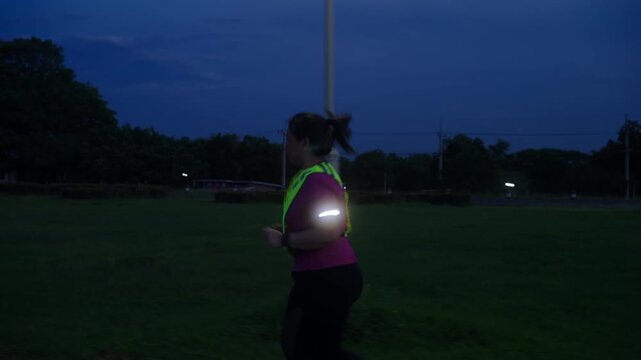 Side view of a middle-aged Asian woman jogging at twilight with reflective gear and an LED arm light for nighttime safety