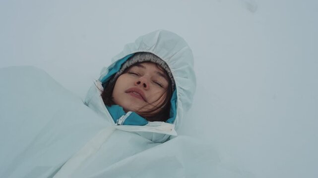 Woman in white hood lying in deep snow, intimate closeup of field medic with windblown hair and faint smile, journal and minimal equipment nearby, cinematic icy light and moody silence convey
