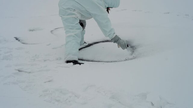 White suited researcher kneels on snowy field examining circular dark crater, collecting samples with gloved hands, overcast sky, frozen wasteland, scattered footprints, post disaster study mood