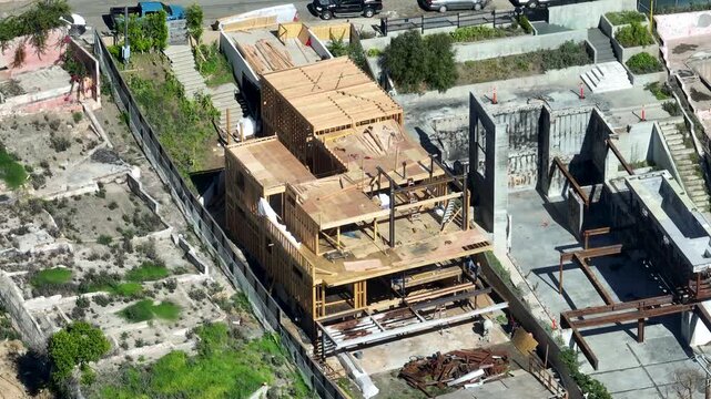 Reconstruction of luxury, wooden frame homes on hillside lots after the January 2025 Palisades wildfires in California - tilt down aerial orbit