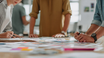 Fototapeta premium Group of creative professionals collaborates on project, reviewing colorful design materials spread across table. atmosphere is focused and dynamic, reflecting teamwork and innovation
