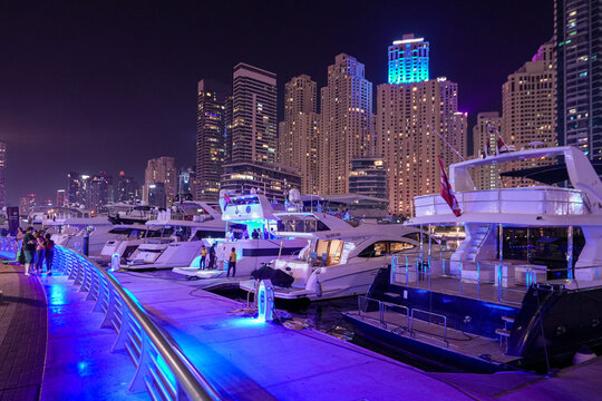 Dubai, United Arab Emirates - 22 April 2023: View of Dubai Marina with luxury yachts docked at the pier and illuminated skyscrapers at night.