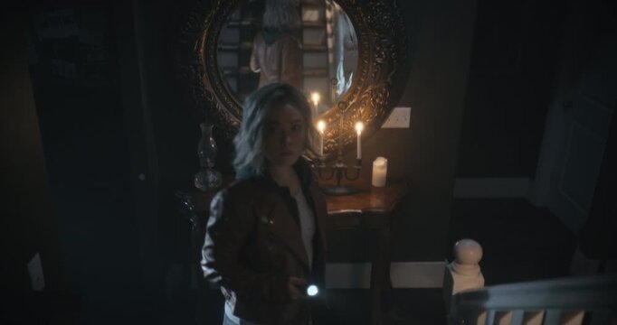 Young woman with flashlight walking up steps of creepy home and being distracted by something - high shot
