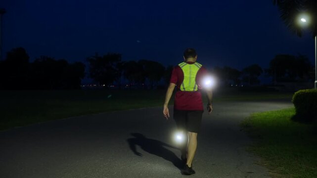 Rear view of a middle-aged Asian man walking home after nighttime jogging with LED safety lights