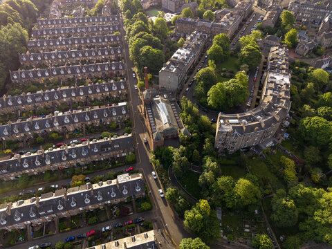 Aerial view of historic terraced houses and lush green gardens along a curved residential street during golden hour Edinburgh, Scotland, United Kingdom.