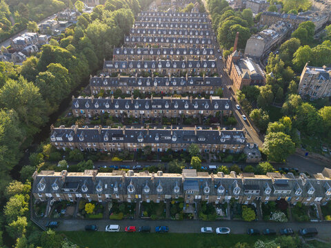 Aerial view of rows of historic stone terraced houses with dormer windows surrounded by lush green trees in the golden hour light in Edinburgh, Scotland, United Kingdom.
