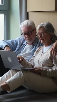 Elderly couple sitting on the floor of their new home, using a laptop to plan and decorate while surrounded by cardboard boxes, enjoying their fresh start and retirement together