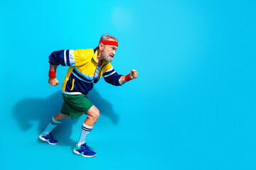 Naklejka premium Senior man sprinting in retro sportswear on bright blue background showing active lifestyle, fitness, energy and playful vintage workout style