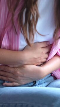 Close-up view of a young woman experiencing a severe stomach ache, pressing her hands on her belly to alleviate the painful cramps caused by indigestion, gastritis, or menstrual period