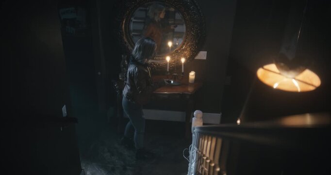 Young woman with flashlight slowly walking through dark, spooky house and being startled by her reflection - high shot