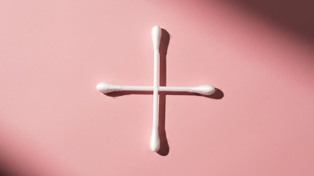 Two cotton swabs arranged in a cross on pink background.