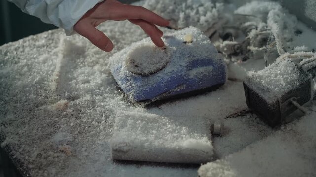 Gloved hand reaching frostcovered telephone on snowdusted desk among scattered papers and ruined electronics, cold blue handset halfburied under crystalline powder, careful inspection for last