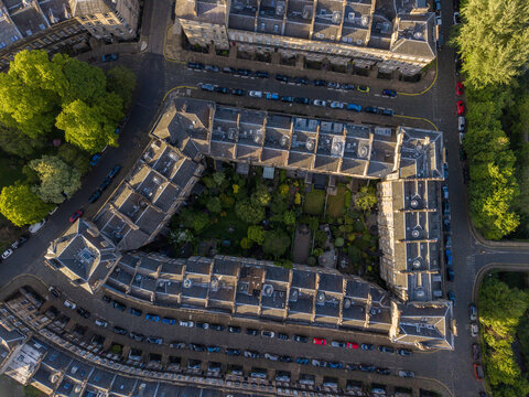 Aerial view of historic stone residential buildings with lush inner gardens and parked cars along the streets in the golden hour light Edinburgh, Scotland, United Kingdom.