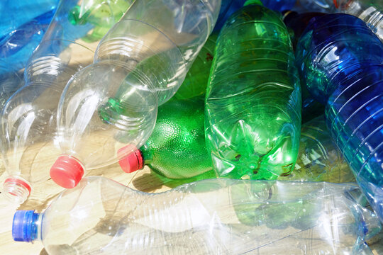 Many different plastic drink bottles on sunlit surface. Demonstrates household waste accumulation patterns, cap-included collection, and increasing pressure on municipal recycling infrastructure.