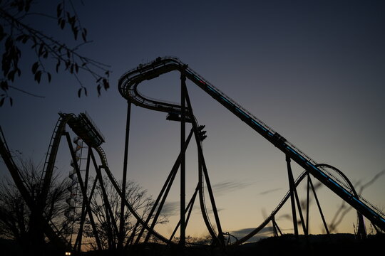 Silhouette of a thrilling roller coaster track in an amusement park against a twilight sunset sky
