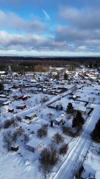 Vertical aerial drone footage moving backward while gaining altitude above a snow-covered countryside village in Northern Europe.